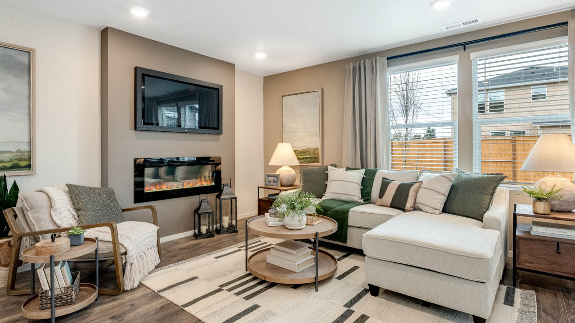 East Park Village great room with laminate flooring, coffee table, rug, rocking chair, white couch, lamp with end table, painting on tan wall, lights, electric fireplace, and windows with blinds