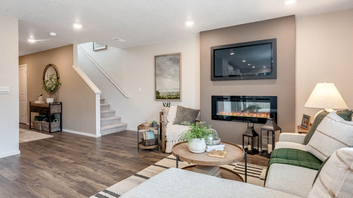 East Park Village great room with laminate flooring, coffee table, rug, rocking chair, white couch, lamp with end table, painting on tan wall, lights, electric fireplace, and windows with blinds, view of entryway with mirror and end table and staircase