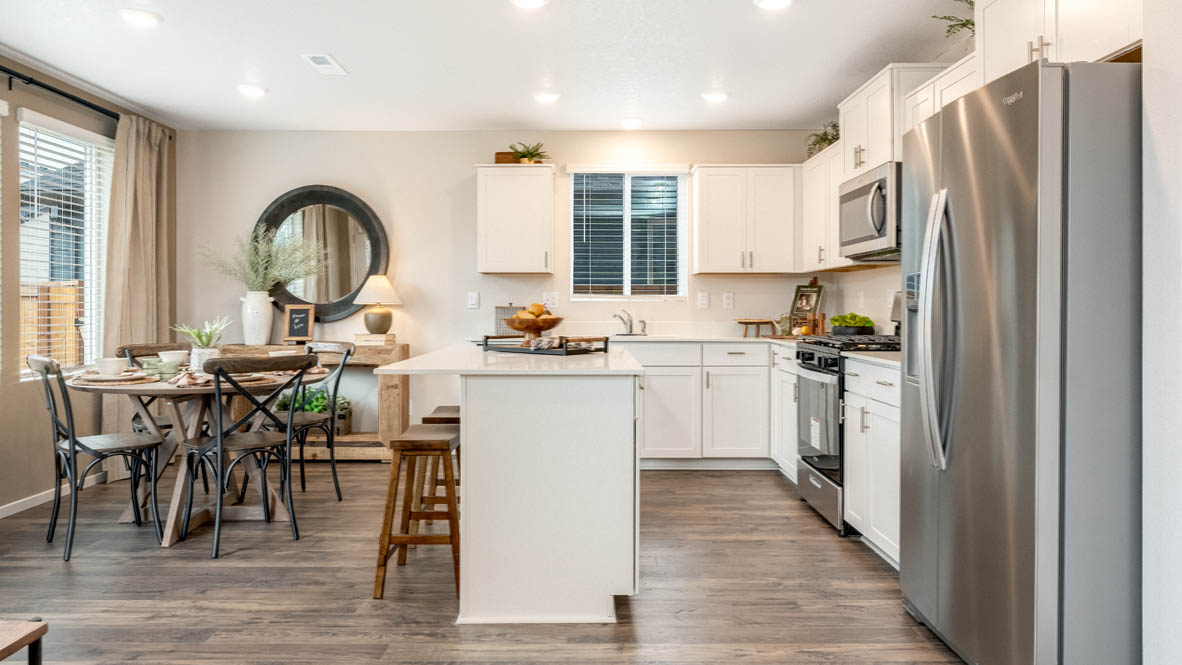 East Park Village kitchen with white quartz countertops, laminate flooring, island with a breakfast bar, shaker style cabinets, windows with blinds, kitchen window, stainless steel appliances