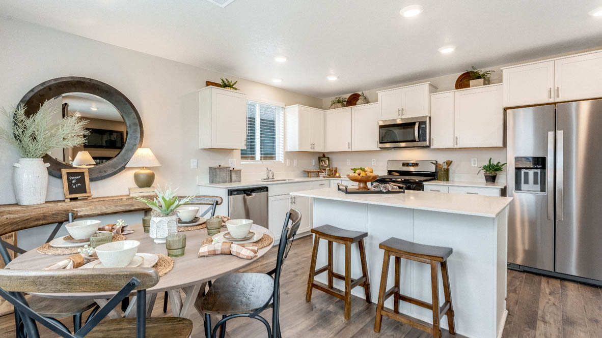 East Park Village kitchen with white quartz countertops, laminate flooring, island with a breakfast bar, shaker style cabinets, windows with blinds, kitchen window, stainless steel appliances