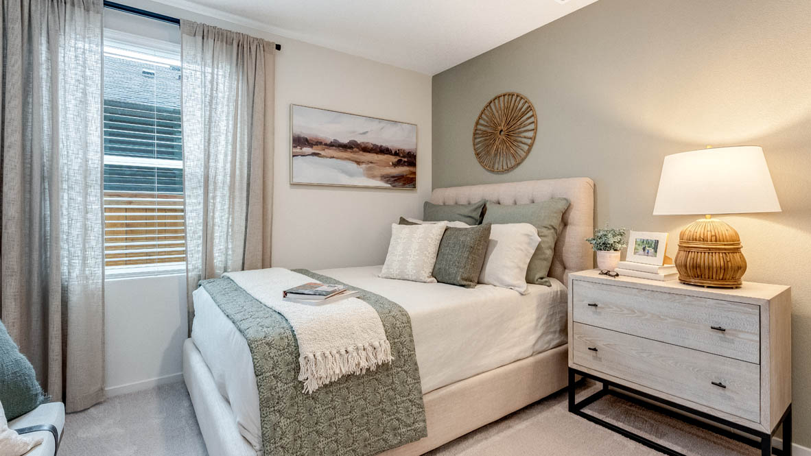 East Park Village bedroom with a window and blinds, bed, end table drawers with lamp, decoration, painting and accent wall, carpet