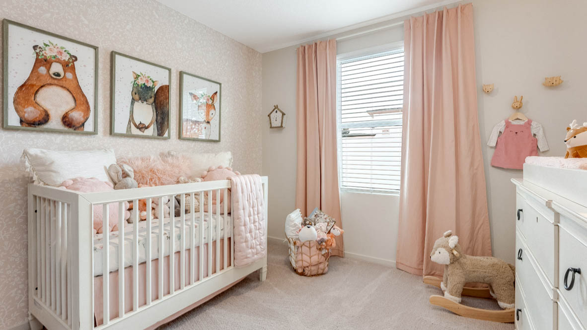 East Park Village bedroom with a white  dresser, circle mirror, painting, pink curtains, carpet, and baby crib