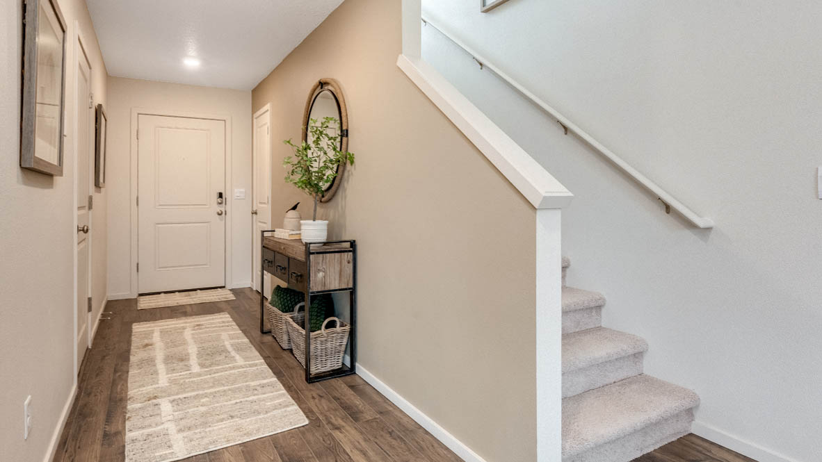 East Park Village entry with a run rug, mirror, end table, paintings, stairs, and white walls with laminate flooring