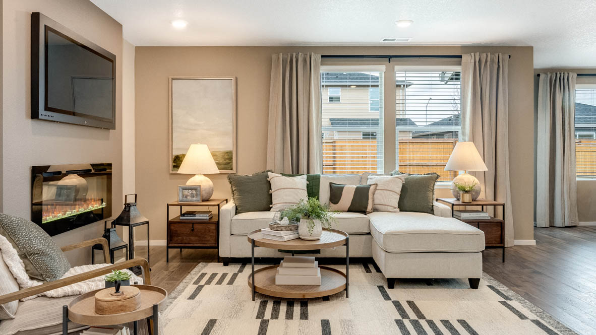 East Park Village great room with laminate flooring, coffee table, rug, rocking chair, white couch, lamp with end table, painting on tan wall, lights, electric fireplace, and windows with blinds