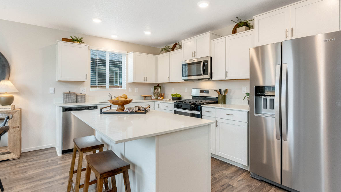 East Park Village kitchen with white quartz countertops, laminate flooring, island with a breakfast bar, shaker style cabinets, windows with blinds, kitchen window, stainless steel appliances