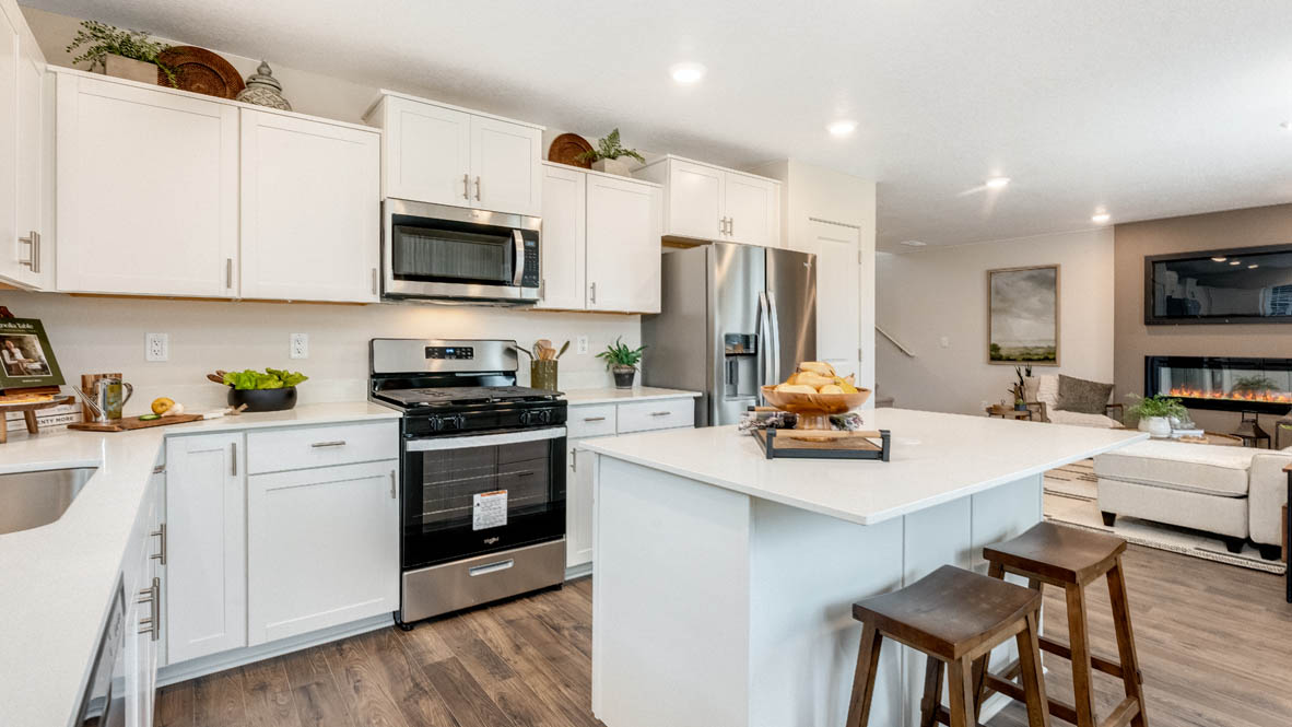 East Park Village kitchen with white quartz countertops, laminate flooring, island with a breakfast bar, shaker style cabinets, windows with blinds, kitchen window, stainless steel appliances