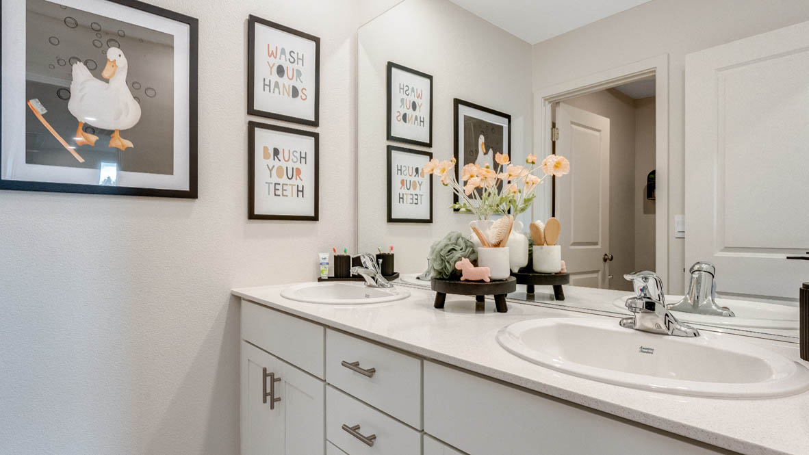 East Park Village bathroom with solid quartz countertops, white cabinets, three paintings, flower plant, mirror