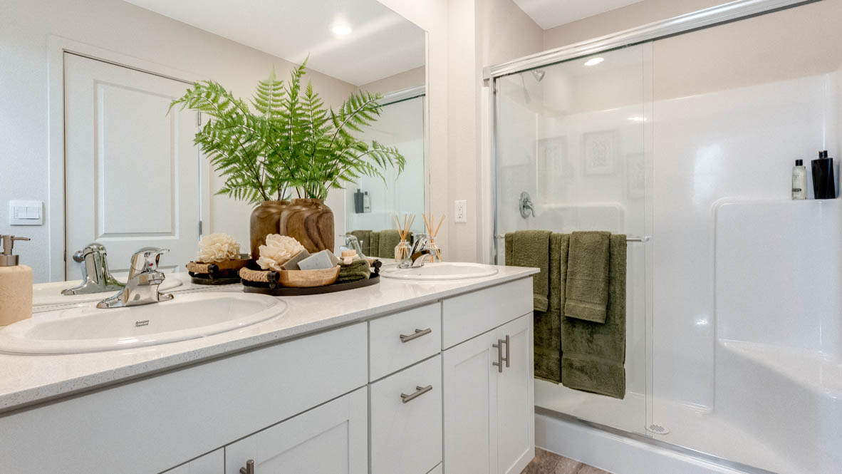 East Park Village Primary bathroom with double vanity, white quartz countertops, plants, white cabinets, walk-in shower with sliding glass door