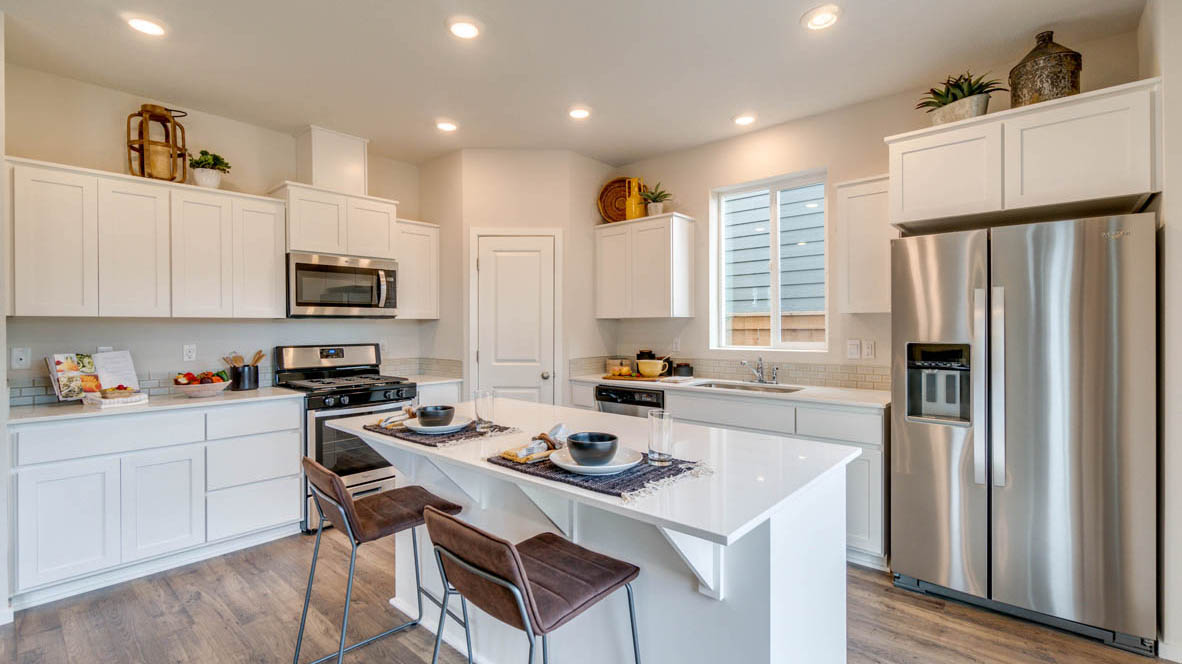 East Park Village Kitchen with white quartz countertops, white shaker cabinets, stainless steel appliances, and an island with two chairs set at it