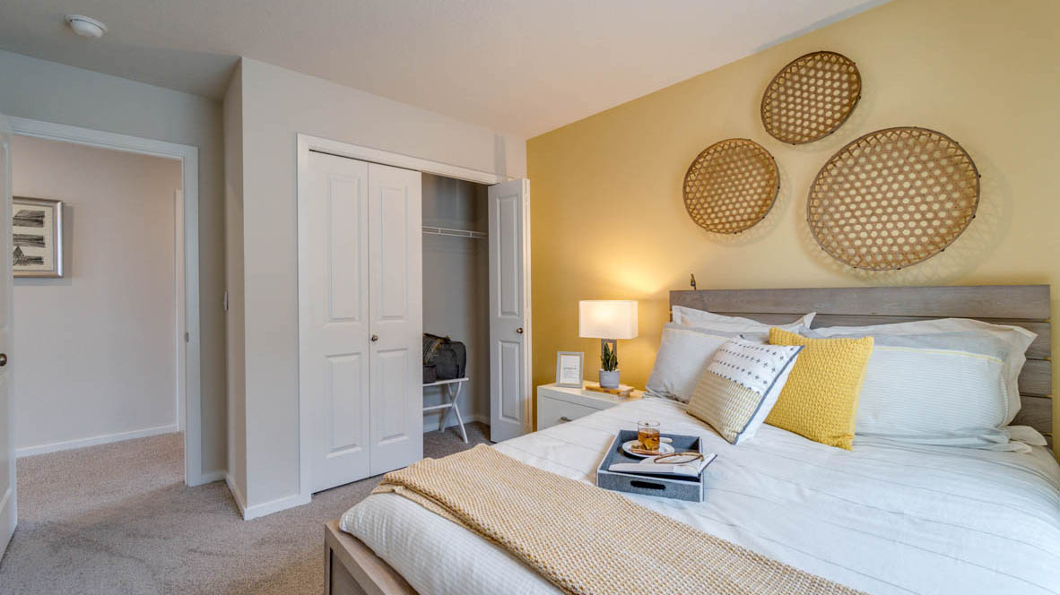 East Park Village Bedroom with yellow accent wall, light wood bed frame, and white, yellow, and gray accents