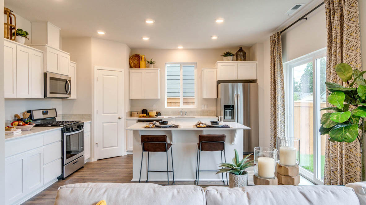 East Park Village Kitchen with white quartz countertops, white shaker cabinets, stainless steel appliances, and an island with two chairs set at it