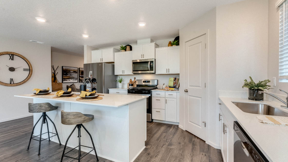 East Park Village Kitchen with island with a breakfast bar, two chairs, stainless steel appliances, white cabinets, laminate flooring, a pantry, and entry in the background
