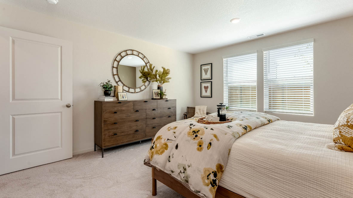 East Park Village Primary bathroom with carpet and a bed with a bedframe, nightstands with lamps, single chair with paintings, windows, and dresser with mirror