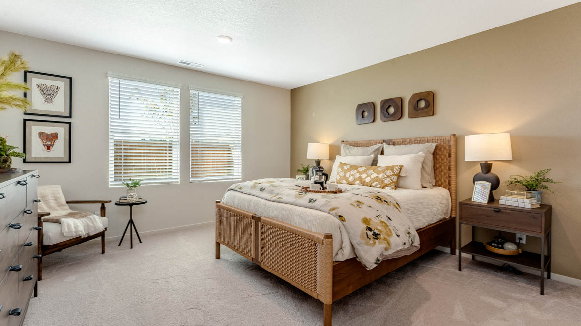 East Park Village Primary bathroom with carpet and a bed with a bedframe, nightstands with lamps, single chair with paintings, windows, and dresser with mirror