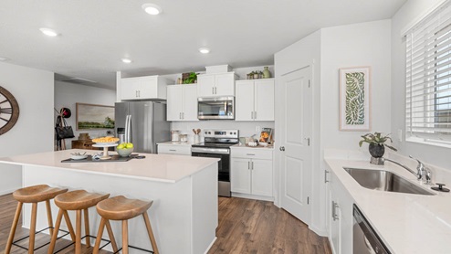 Addysen Park kitchen with island and white shaker style cabinets, white quartz countertops, laminate flooring, and staged furniture