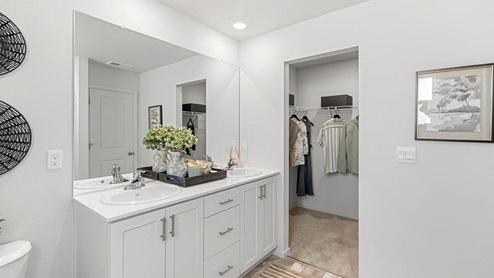 Addysen Park primary bathroom with double sink vanity and white shaker style cabinets and white solid surface countertops and walk in closet