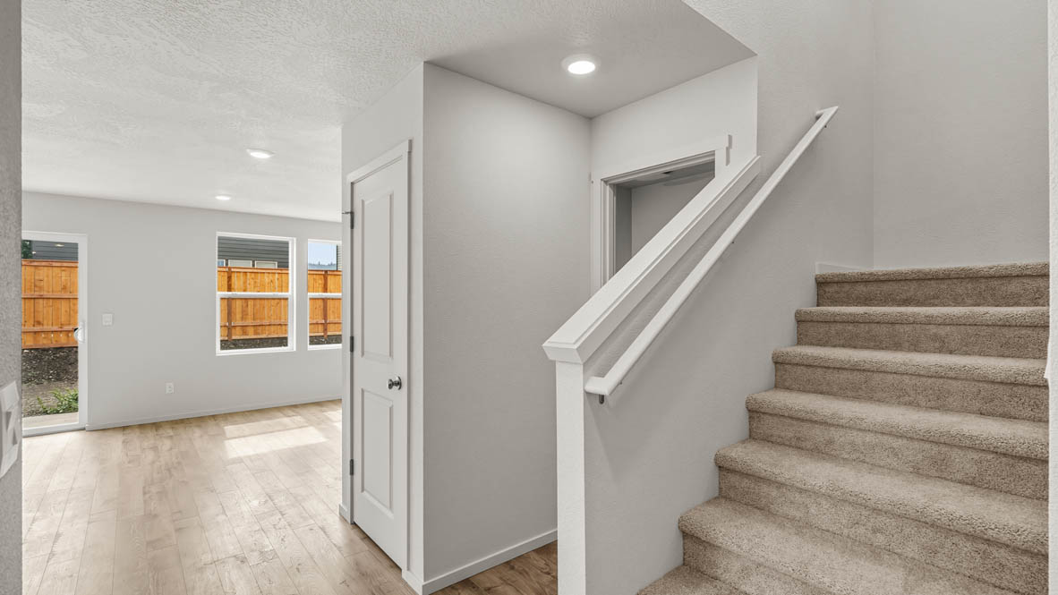 Addysen Park Entry with carpeted stairs, painted white stair railing, laminate flooring, and dining room in the background with windows and sliding glass door