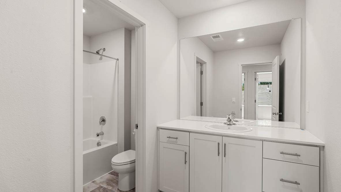 Addysen Park secondary bathroom wit quartz countertops, mirror, toilet, and shower tub