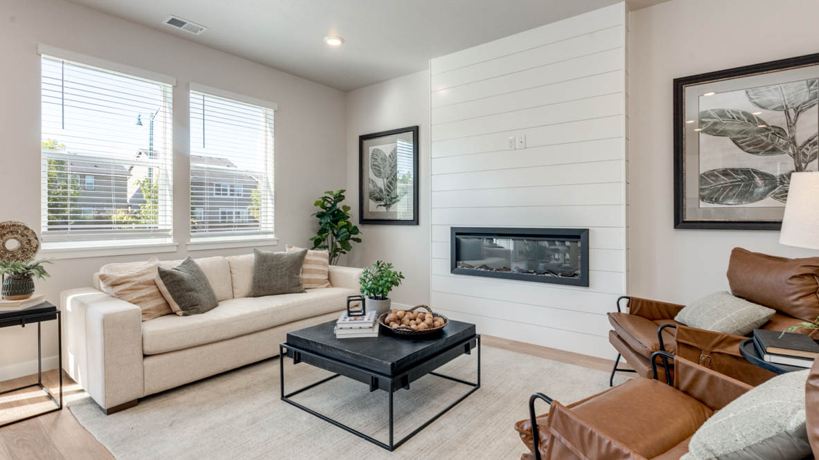 Avery Terrace great room with laminate flooring, white carpet, a brown chair, entertainment center, white couch, glass coffee table, plants, paintings, and a tv