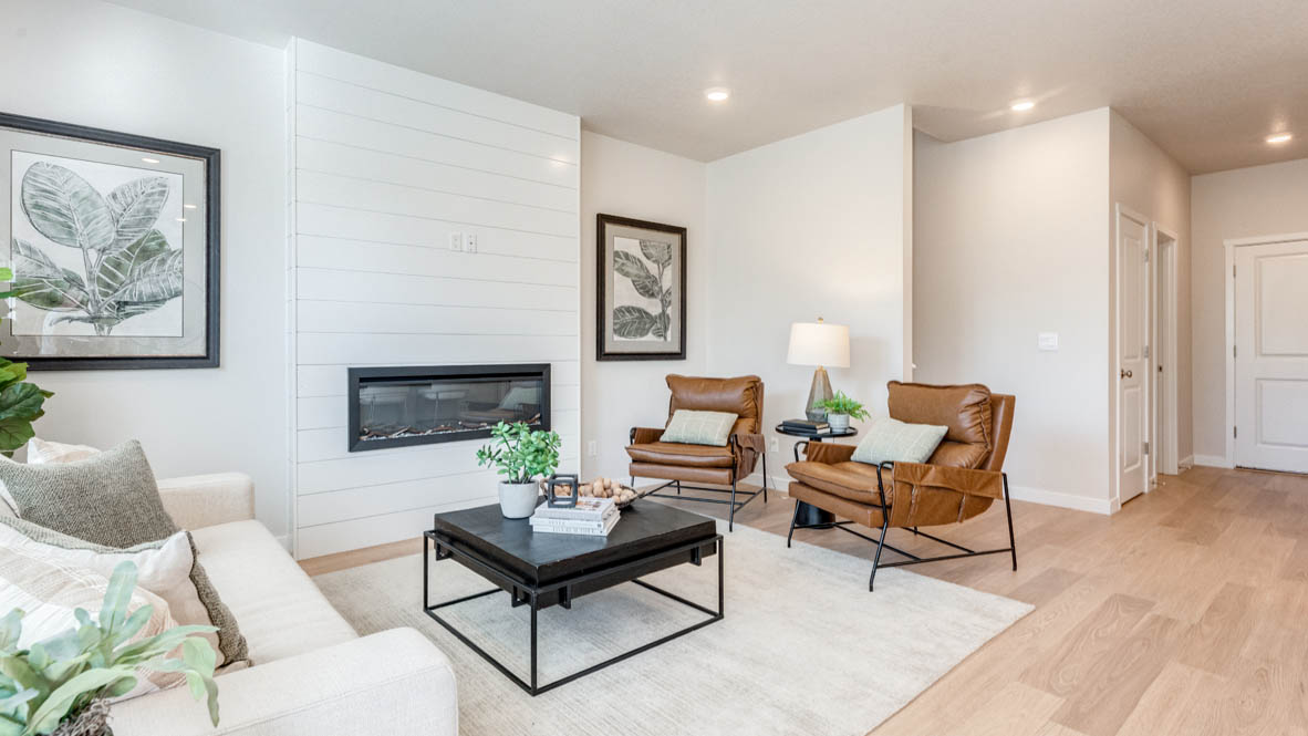 Avery Terrace great room with laminate flooring, white carpet, a brown chair, entertainment center, white couch, glass coffee table, plants, paintings, and a tv