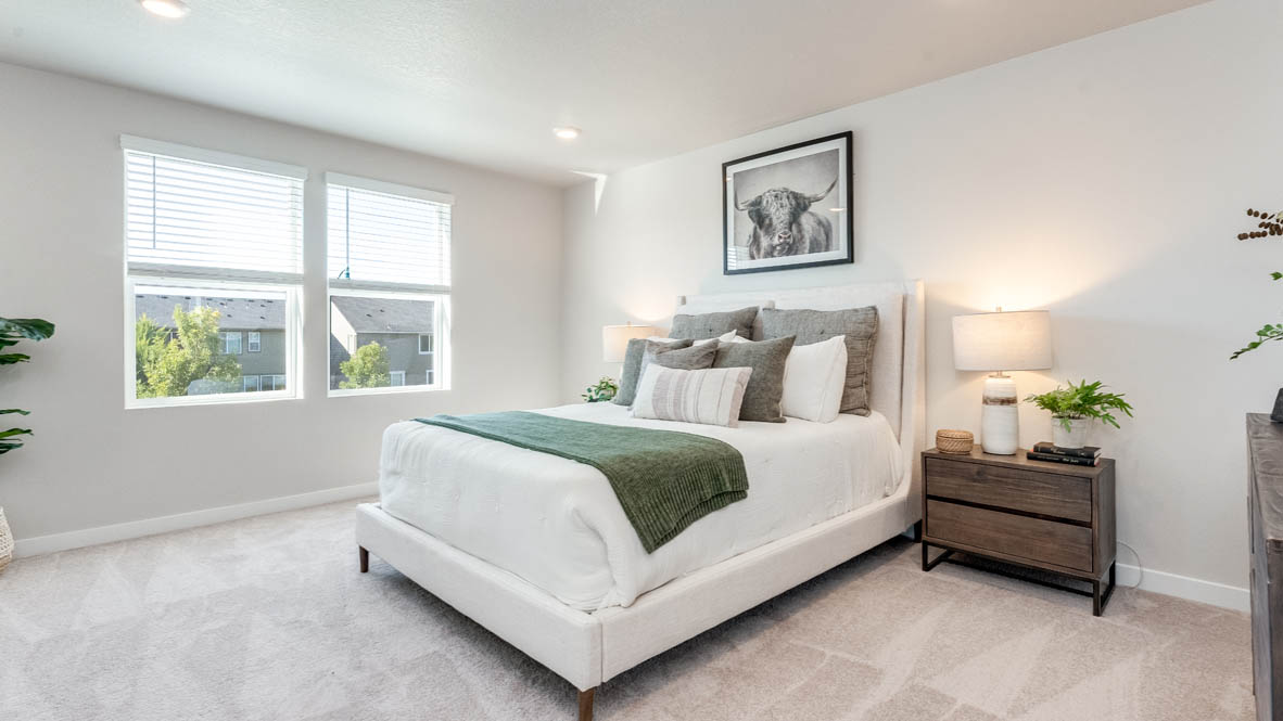 Avery Terrace Primary bedroom with carpet and a bed with a white bedframe, two end tables, two lamps, pillows, windows, and plants