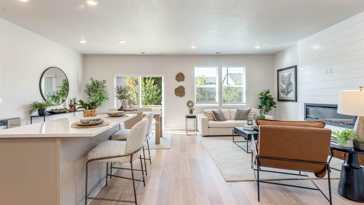 Avery Terrace great room with laminate flooring, white carpet, coffee table, plants, white couch with pillows, and dining room with a rug and tablet set and chairs