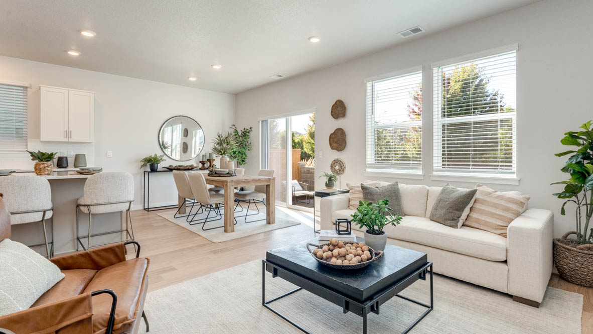 Avery Terrace great room with laminate flooring, white carpet, coffee table, plants, white couch with pillows, and dining room with a rug and tablet set and chairs
