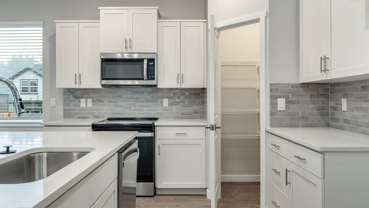 Kitchen with shaker cabinets, quartz counters, stainless steel appliances, pantry, and an island with a breakfast bar