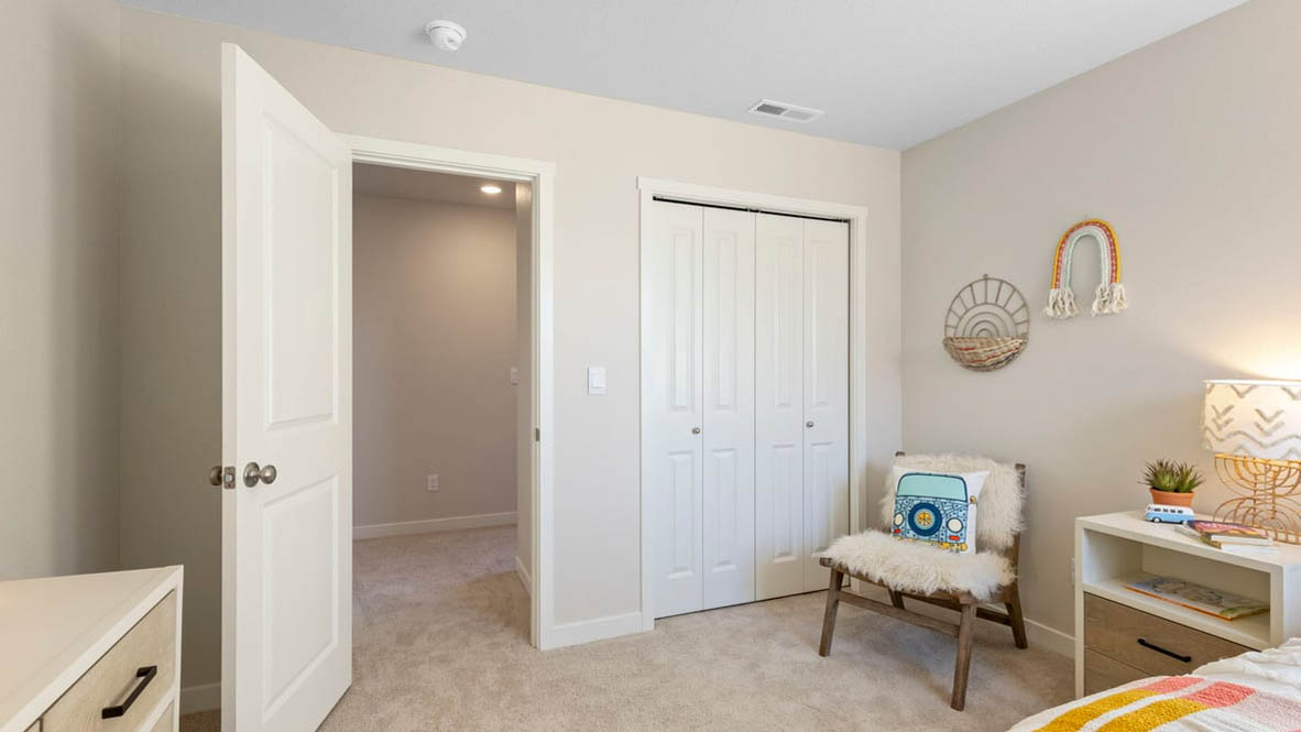 Avery Terrace Bedroom with a bed with sheets, light stained bed frame, end table with a lamp, paintings, and a closet
