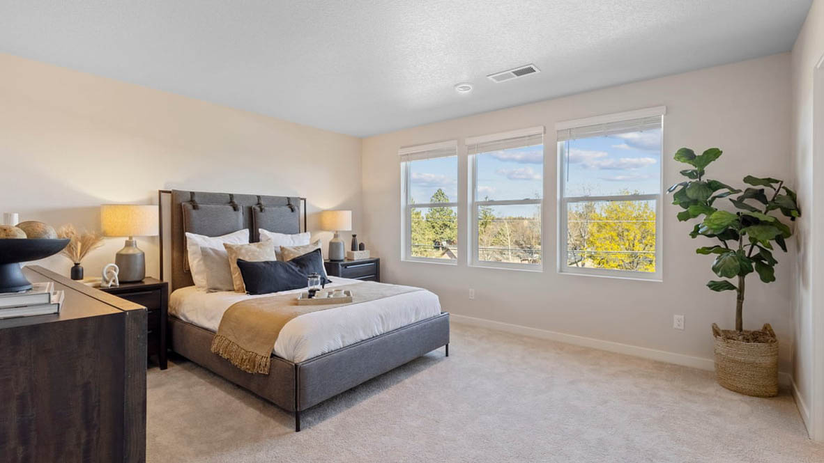 Avery Terrace Primary bedroom with carpet and a bed with a white bedframe, two end tables, two lamps, pillows, windows, and plants