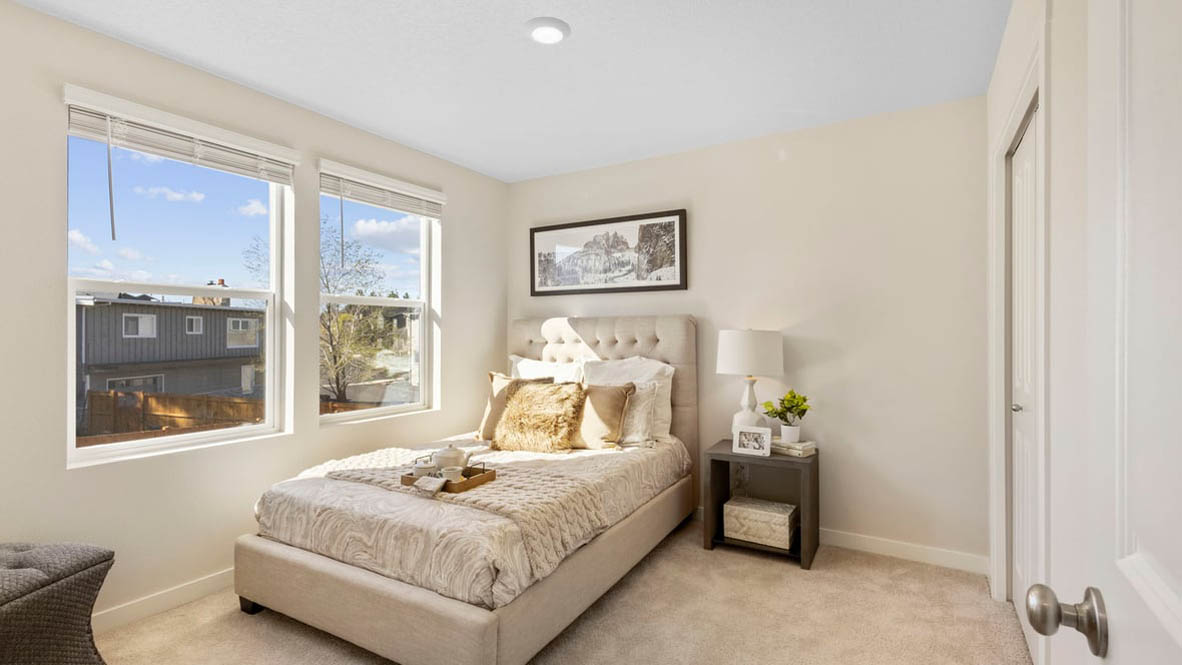 Avery Terrace Bedroom with a bed with sheets, light stained bed frame, end table with a lamp, paintings, and a window