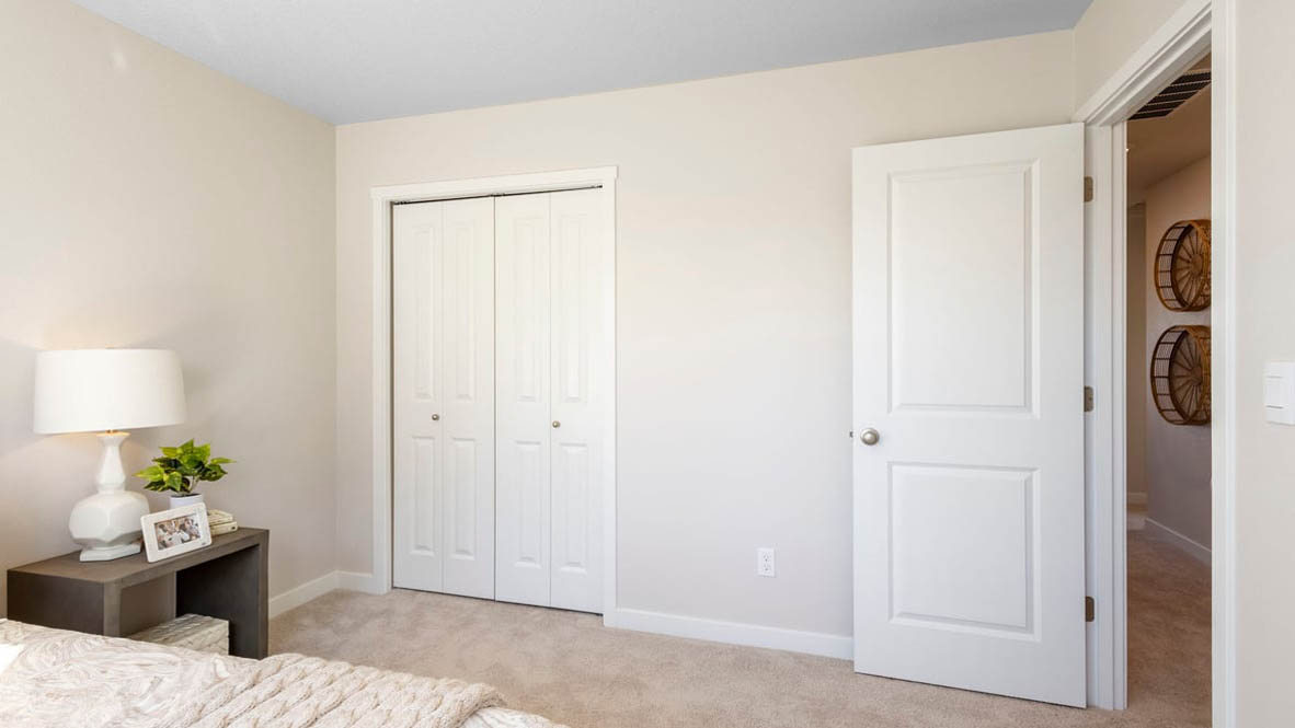 Avery Terrace Bedroom with a bed with sheets, light stained bed frame, end table with a lamp, paintings, and a closet