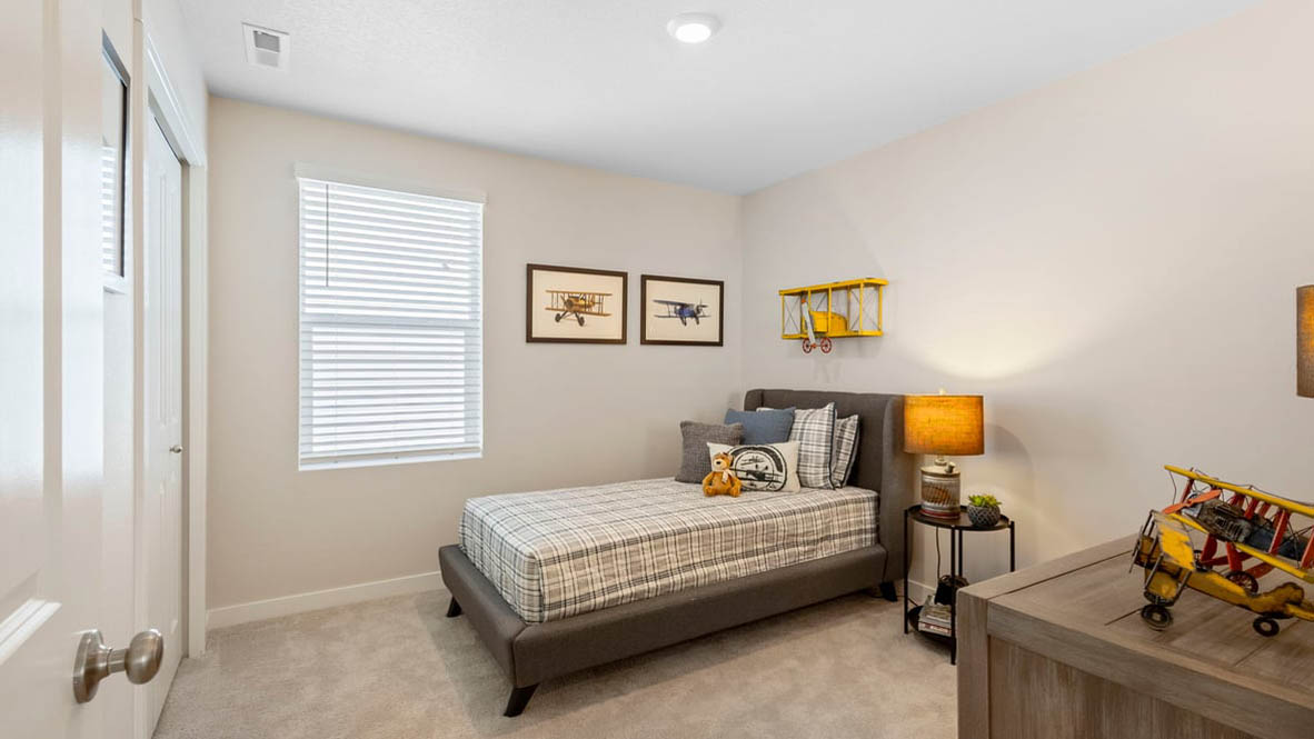 Avery Terrace Bedroom with a bed with sheets, light stained bed frame, end table with a lamp, paintings, and a window