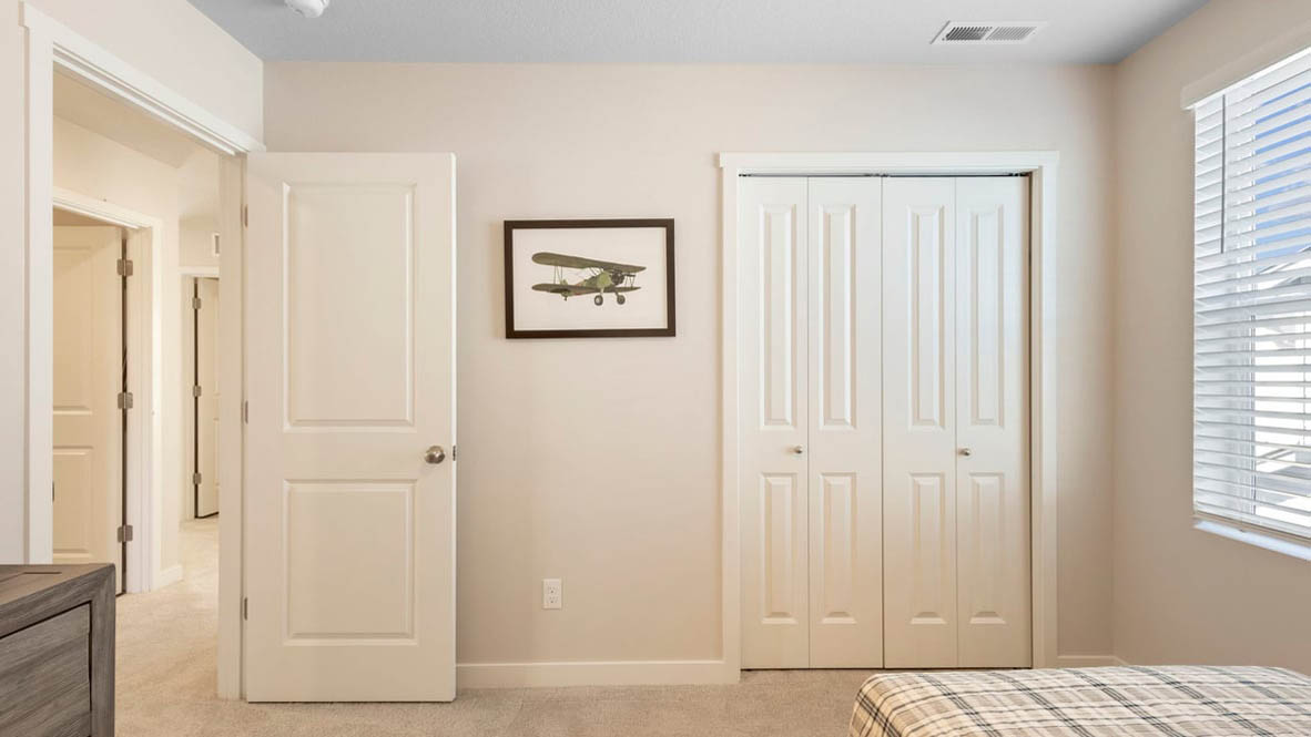 Avery Terrace Bedroom with a bed with sheets, light stained bed frame, end table with a lamp, paintings, and a closet