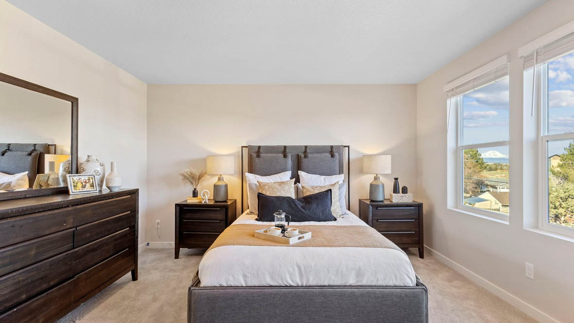 Avery Terrace Primary bedroom with carpet and a bed with a white bedframe, two end tables, two lamps, pillows, windows, and plants