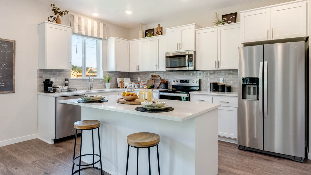 Avery Terrace Kitchen with two stools seated at the island, white quartz countertops, white shaker style cabinets, and stainless steel appliances