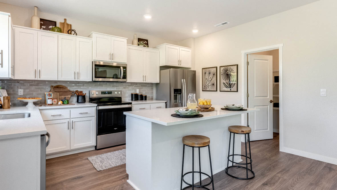 Avery Terrace Kitchen with two stools seated at the island, white quartz countertops, white shaker style cabinets, and stainless steel appliances