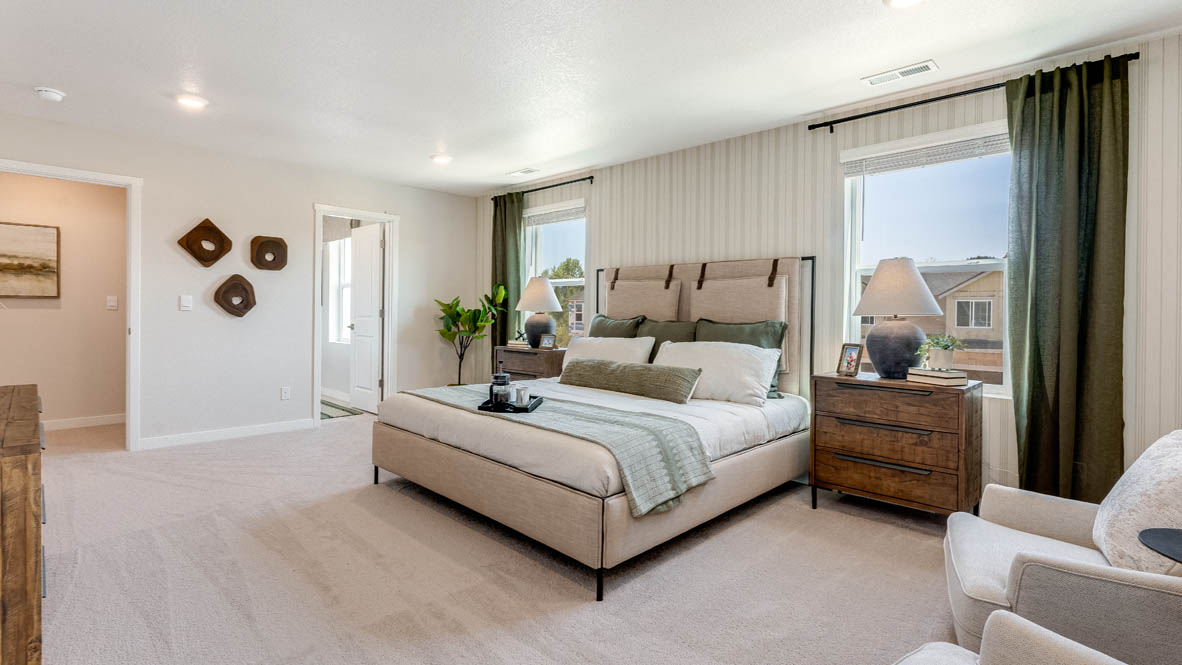Avery Terrace Primary bedroom with a striped wallpaper accent wall, large bed with two accent chairs against once wall and two side tables one on either side of the bed. Carpeted flooring and green window drapes