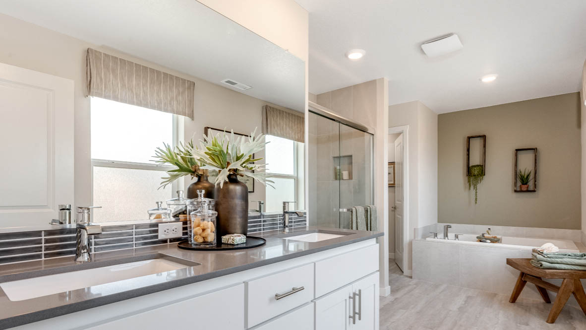 Avery Terrace Primary bedroom with a striped wallpaper accent wall, large bed with two accent chairs against once wall and two side tables one on either side of the bed. Carpeted flooring and green window drapes