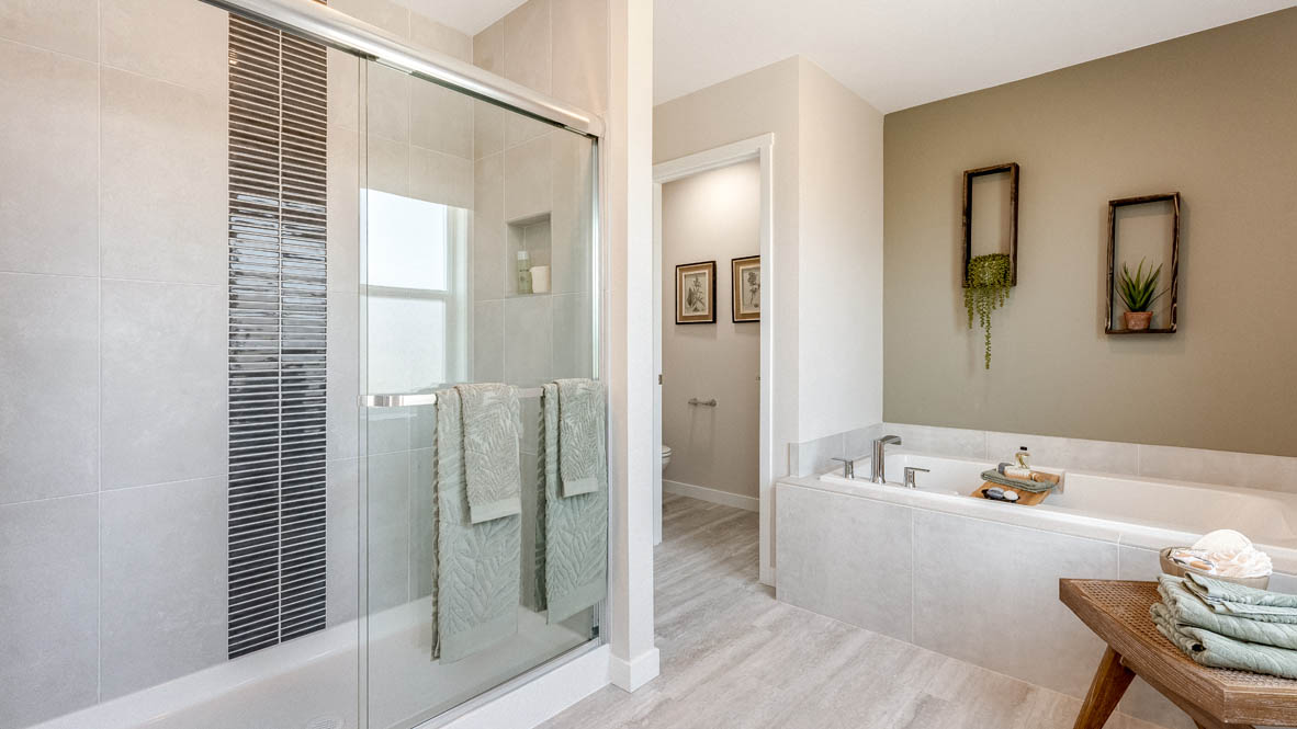 Avery Terrace Primary bedroom with a striped wallpaper accent wall, large bed with two accent chairs against once wall and two side tables one on either side of the bed. Carpeted flooring and green window drapes