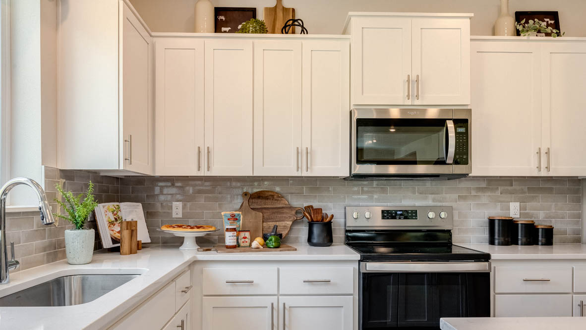 Avery Terrace Kitchen with two stools seated at the island, white quartz countertops, white shaker style cabinets, and stainless steel appliances