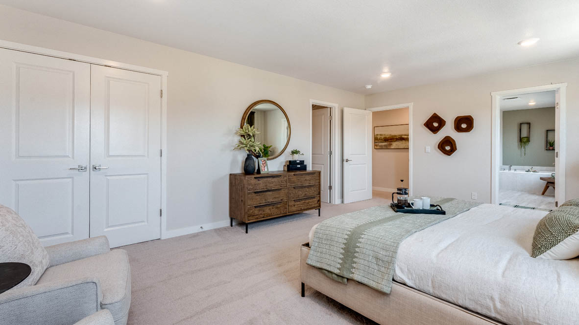 Avery Terrace Primary bedroom with a stripped wallpaper accent wall, large bed with two accent chairs against once wall and two side tables one on either side of the bed. Carpeted flooring and green window drapes