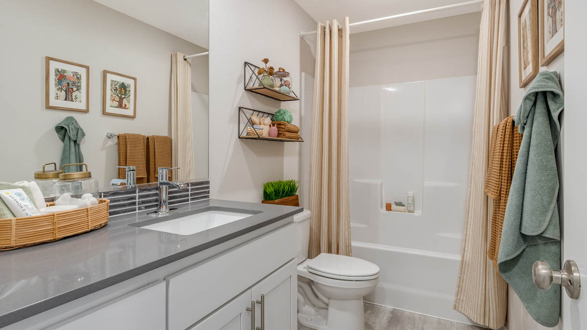 Avery Terrace secondary bathroom with solid surface countertops, toil, mirror, bathtub, hanger with towels,