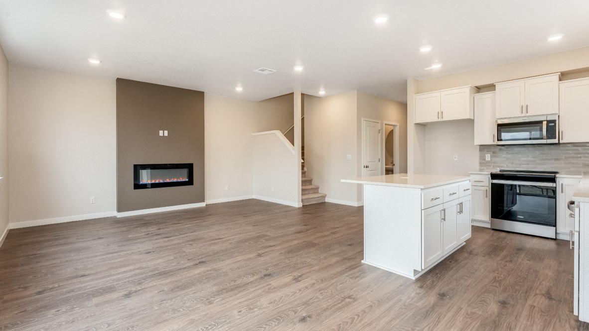 Avery Terrace kitchen and great room with laminate flooring, an island with quartz countertops, soft closed cabinets, electric fireplace with accent wall, sliding glass door, two windows