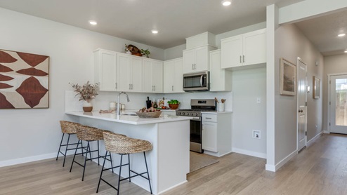 Gordon Creek Pointe Kitchen with stool chairs, quartz countertops, island peninsula, stainless steel appliances, white cabinets, laminate flooring, and decorative painting