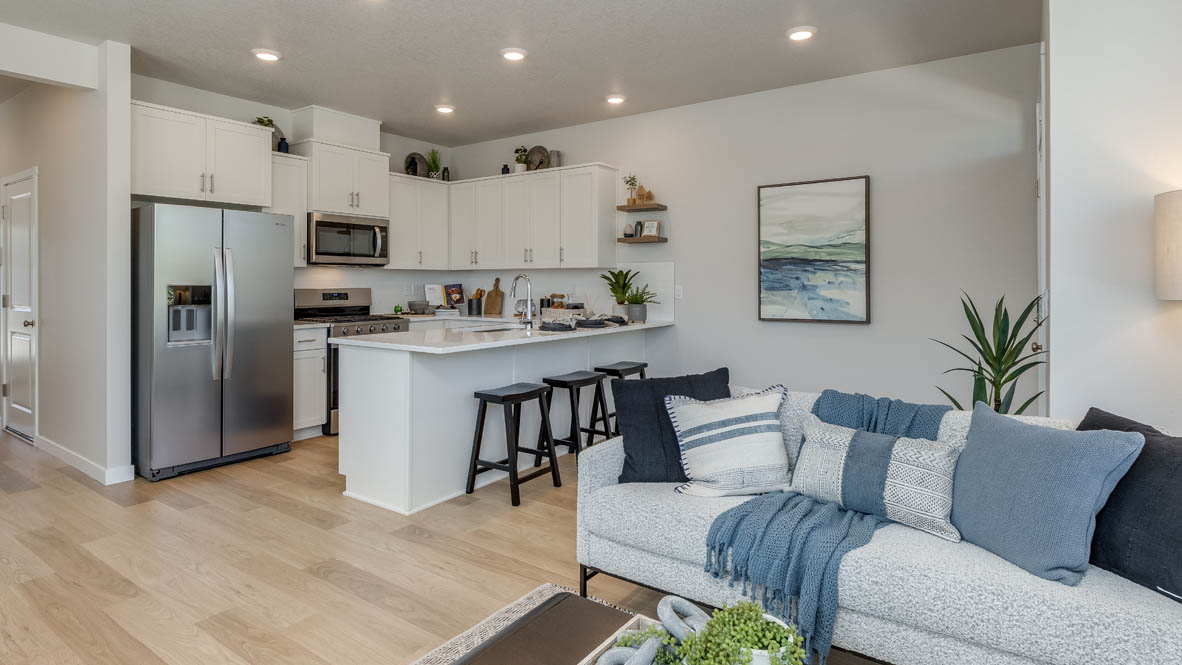 Gordon Creek Pointe Great room with couch and blue pillows, laminate flooring, coffee table, and the kitchen in the background