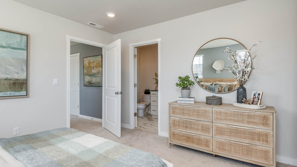 Gordon Creek Pointe Primary bedroom with carpet, dresser with plants, circle mirror, and the bathroom in the background