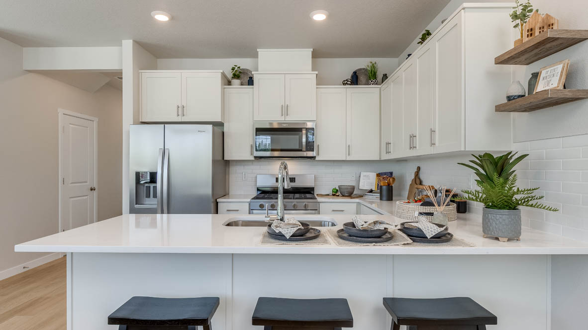 Gordon Creek Pointe Kitchen with a peninsula, barstool chairs, laminate flooring, quartz countertops, stainless steel appliances, drawers, and the dining room in the background
