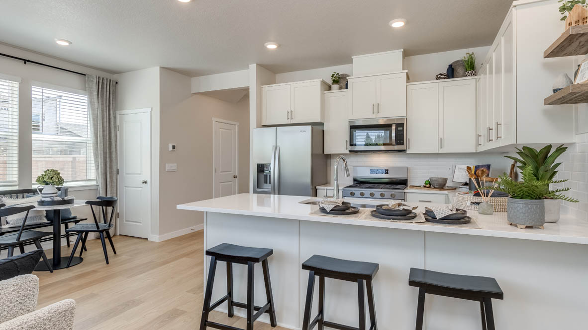 Gordon Creek Pointe Kitchen with a peninsula, barstool chairs, laminate flooring, quartz countertops, stainless steel appliances, drawers, and the dining room in the background