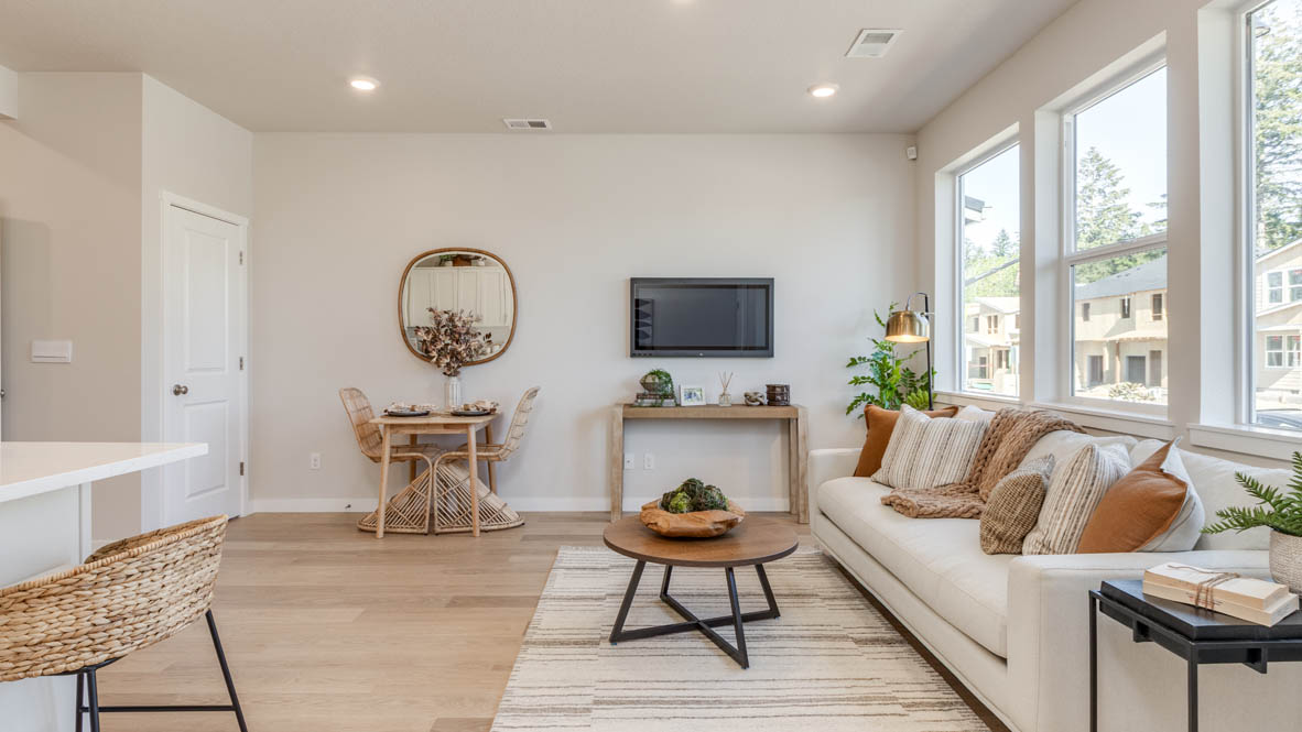 Gordon Creek Pointe Great Room with a coffee table, white couch with pillows, windows, a tv and entertainment center, a plant, with the dining table and circle mirror in the background